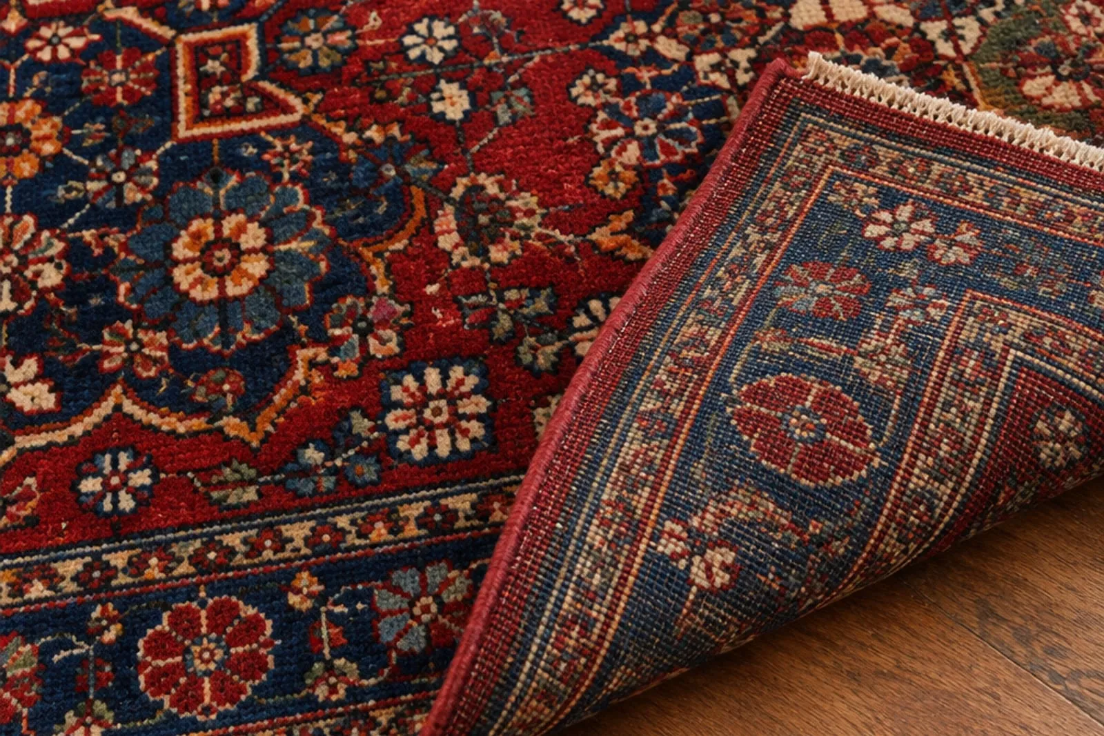 The corner of a hand-knotted Oriental rug folded back to show the knotted reverse beside its patterned face